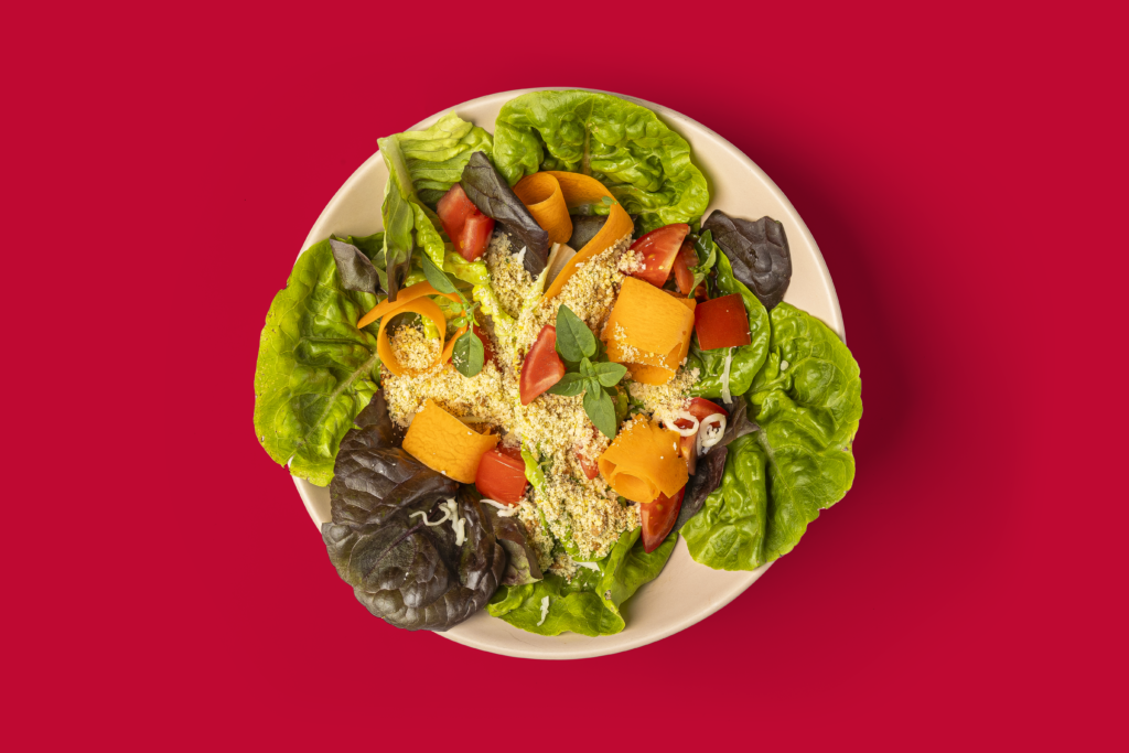 Salada crocante com Farofa Caldo Bom, folhas verdes e tomates.