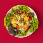 Salada crocante com Farofa Caldo Bom, folhas verdes e tomates.